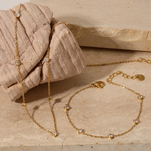 Elegant gold zircon necklace and bracelet set displayed on a textured stone background