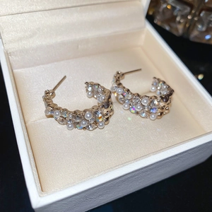 Macro shot of elegant gold C-shape hoop earrings with crystal and pearl inlay detailing
