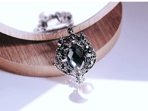 Detailed macro view of vintage baroque brooch with green emerald gem and pearl drop
