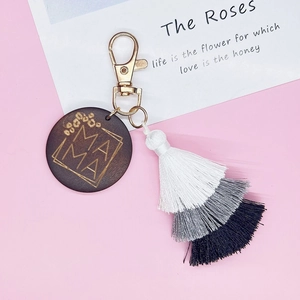 Detail of wooden MAMA keychain with multi-color tassels and golden hardware on pink background