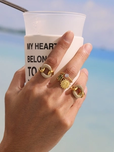 Detail of stacked gold-plated rings with green zircon and sun charm on hand