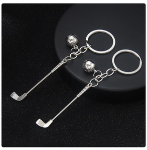 Close-up of silver metal golf club and ball keychain on premium black textured background