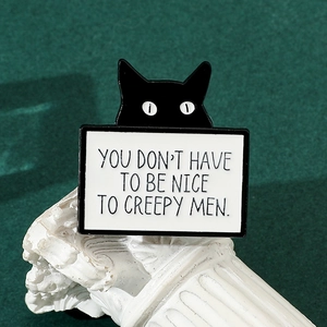 Detail of creative black cat enamel pin with social quote on green velvet background