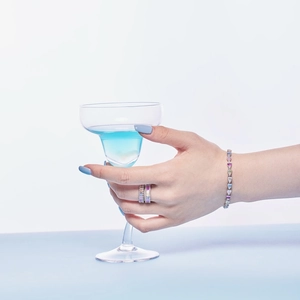 Close-up of a silver bracelet with colorful zircons worn by a model holding a blue cocktail