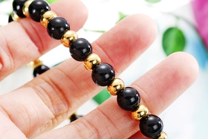 Gros plan d'un bracelet de perles noires et dorées avec une croix rétro porté au poignet