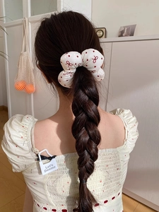 White scrunchie with red hearts and bows worn on a braided hairstyle in soft light