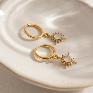 Close-up of gold starburst earrings with white opal stone and rhinestones on ceramic tray