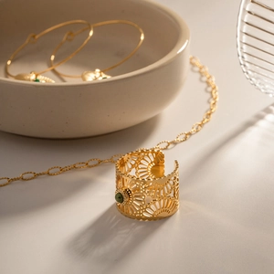 Detailed view of hollow gold-plated ring with inlaid green gemstone on ceramic bowl