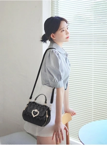 Detail of black pleated bucket bag with gold heart crown buckle and wavy quilting