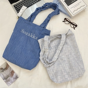 Flat lay of checkered canvas tote bags with embroidered text and ruffled handles