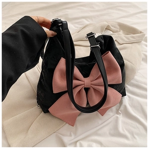 Detailed shot of a black suede handbag featuring a large pink bow and leather shoulder strap