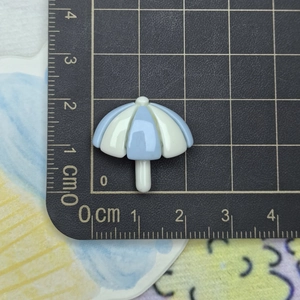 Close-up of a 2cm blue and white resin umbrella charm on a measurement scale