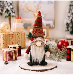 Close-up of Christmas gnome with knitted hat holding a candy cane and pine branch