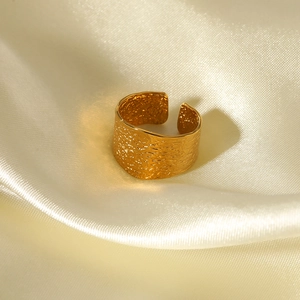 Golden wide C-shaped stainless steel ring with hammered texture on beige silk background