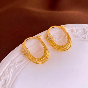 Dettaglio macro di orecchini placcati in oro a forma di U con zirconi su un piatto ceramica