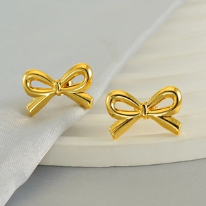 Polished gold bow earrings made of stainless steel displayed on a white textured stand