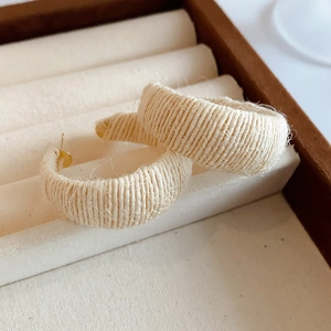 Detail view of beige woven fabric C-shaped earrings on jewelry box padding