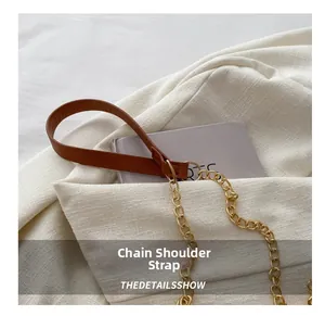 Detail of a brown leather shoulder strap with a chunky gold metal chain on a crossbody bag