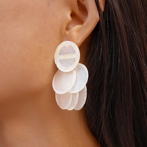 Detail of white translucent layered circular shell drop earrings on a fashion model