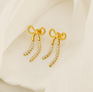 Detail shot of golden bow earrings with sparkling long tassel chains on white fabric