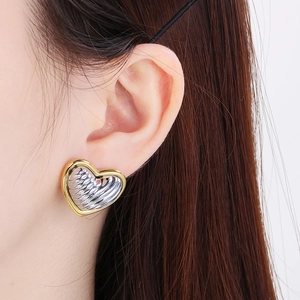 Macro detail of 18K gold plated heart earrings with silver rippled texture on model