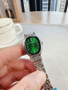 Detailed close-up of oval green dial quartz watch with silver steel band on wrist