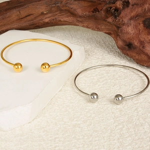 Polished gold and silver adjustable open bangles displayed on natural stone and wood