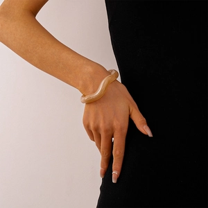 Macro detail of wave-shaped beige acrylic bangle showing resin texture on a wrist