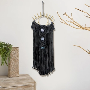 Detail of dark grey woven wall hanging featuring a golden metal eye and natural stones