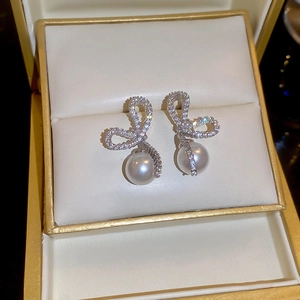 Macro shot of silver bow earrings with sparkling cubic zirconia and a round white pearl