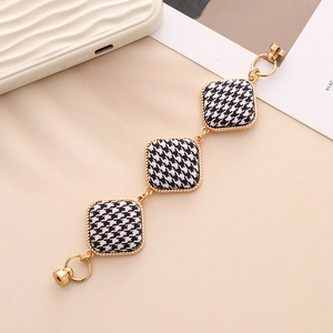 Detail of houndstooth fabric charms with gold frames on a stylish accessory chain