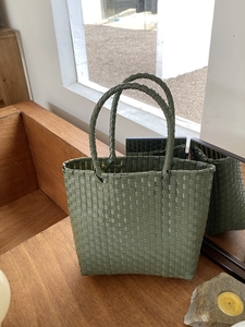 Close-up of green woven straw tote bag texture on wooden furniture in natural sunlight