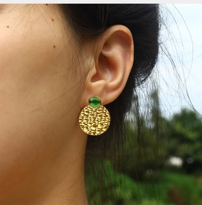 Close-up of vintage golden hammered round earrings with green cat-eye stone on ear