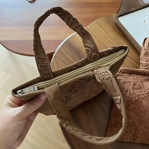 Close-up of vintage brown suede tote with floral embroidery and gold zipper detail