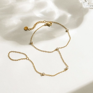 Detail of gold slave bracelet with five white zircons on a rippled background