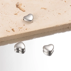 Polished heart shaped stainless steel beads for DIY jewelry making on stone background