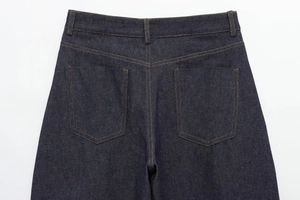 Detail of dark blue denim jeans showing back pockets and orange stitching accents