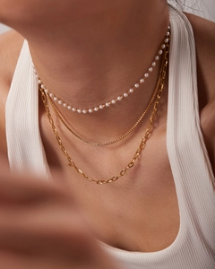 Detailed close-up of a triple-layered gold necklace with pearls and paperclip chains