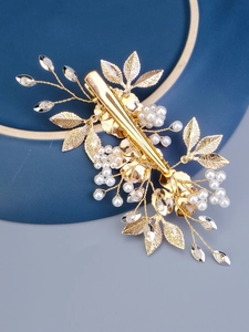 Detail of golden floral hair clip with white pearls and rhinestones on a blue plate