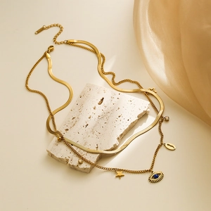 Double-layered gold evil eye necklace with butterfly and star pendants on travertine stone