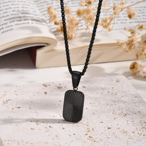 Close-up of black rectangular pendant with sunburst texture on a steel ball chain