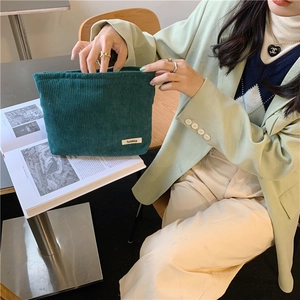 Detail of dark green corduroy makeup bag featuring a minimalist brand logo label