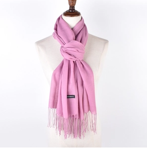 Detail of pink faux cashmere scarf fringe and black product label on a white mannequin