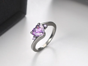 Macro shot of silver ring with heart-shaped purple zircon and polished metal band