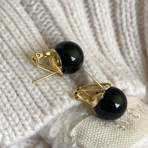 Detailed close-up of gold metal earrings with black onyx bead on a knit fabric background