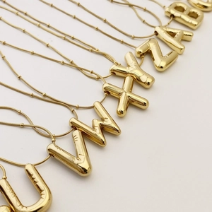 Detail of gold bubble letter pendants with ball chain showing the polished metallic surface