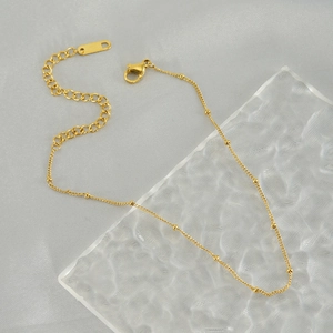 Elegant gold titanium steel anklet with delicate bead chain on a textured glass stand