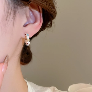 Close-up of a model wearing C-shaped earrings with white enamel and colorful dots