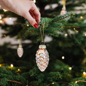 Christmas pinecone ornament in rose gold with silver glitter hanging on a green Xmas tree