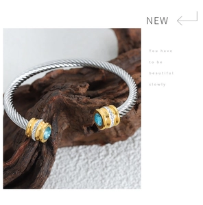 Detail of silver cable bangle featuring a light blue gemstone and gold-toned finish